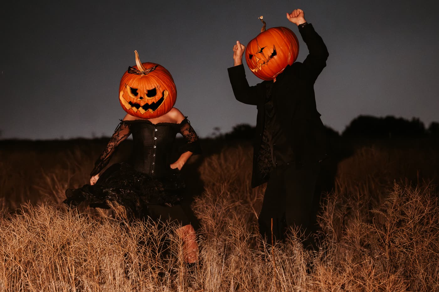 Themed couple portrait, two figures with pumpkin heads at twilight in a field